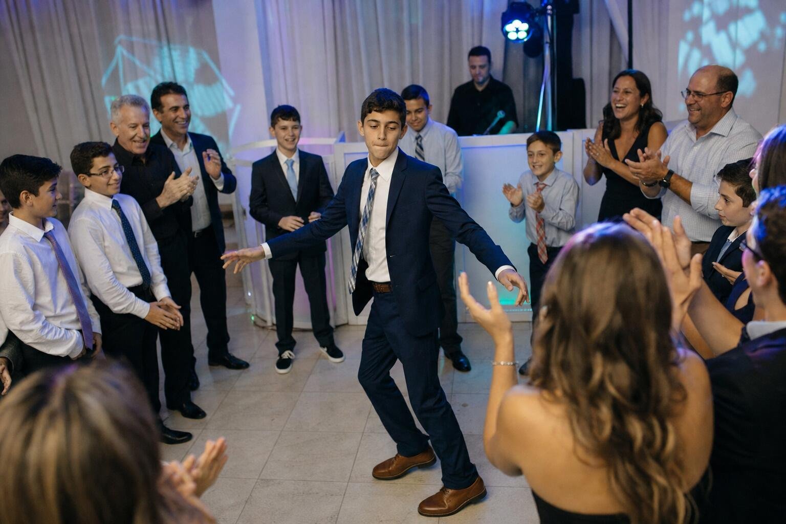 Family and friends dancing in a circle around a teen at a Bar Mitzvah party